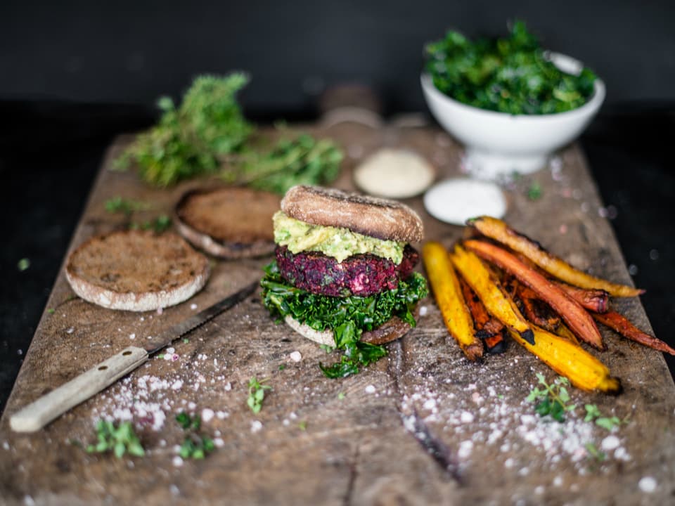Eine Holzplatte mit Karottenpommes und einem selbstgemachten Burger mit Randen und Salat.