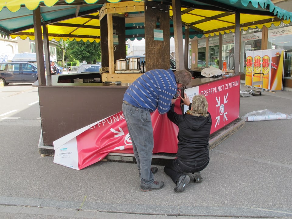 Zwei Leute befestigen Plakate an einem Infostand