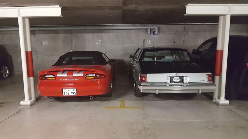 Ein Camaro SS und ein Cadillac Seville stehen nebeneinander in einer Garage.