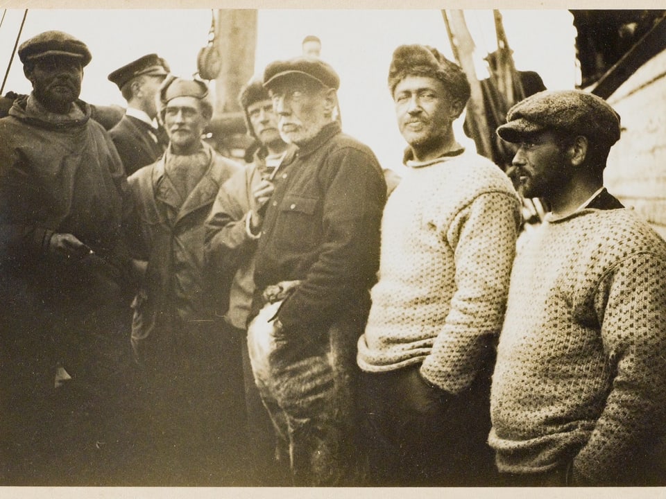 Vergilbte Schwarzweiss-Aufnahme: Männer stehen auf Schiff.