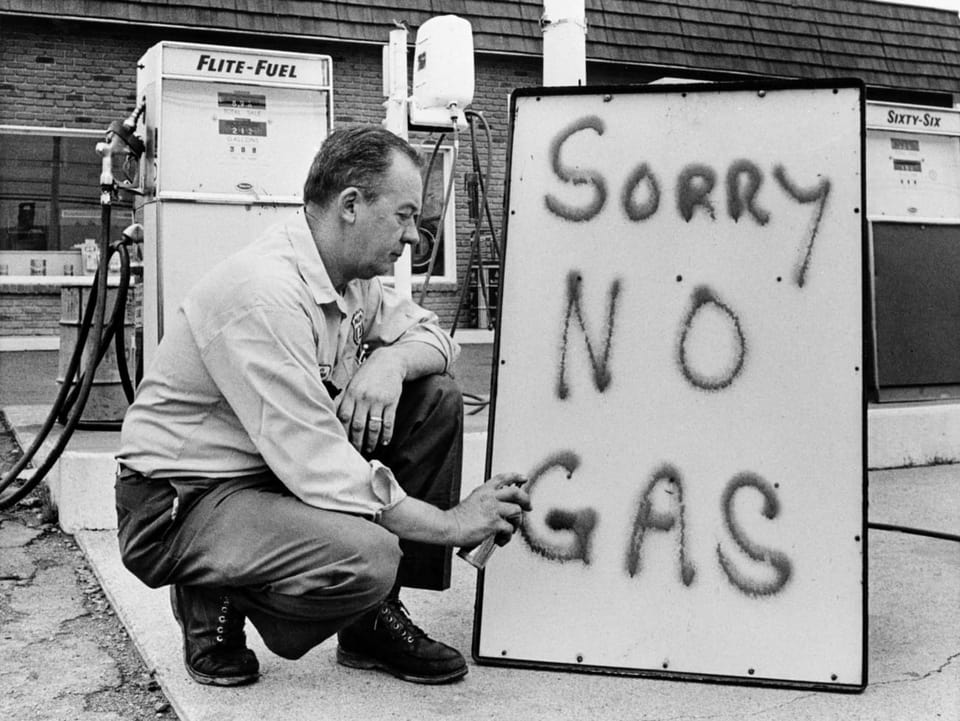 Ein Mann schreibt auf eine Tafel, dass er kein Benzin mehr verkaufen kann.