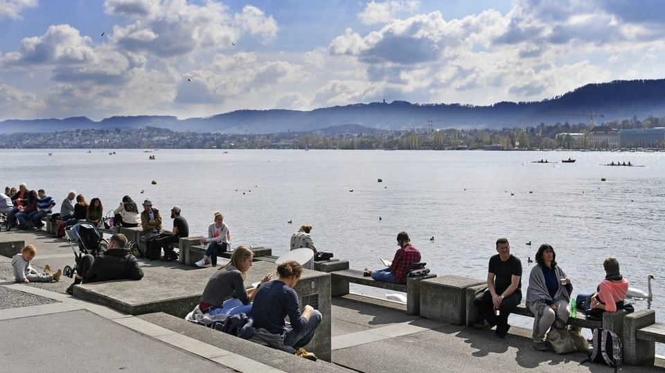 Menschen sitzen am Ufer des Zürichsees. 