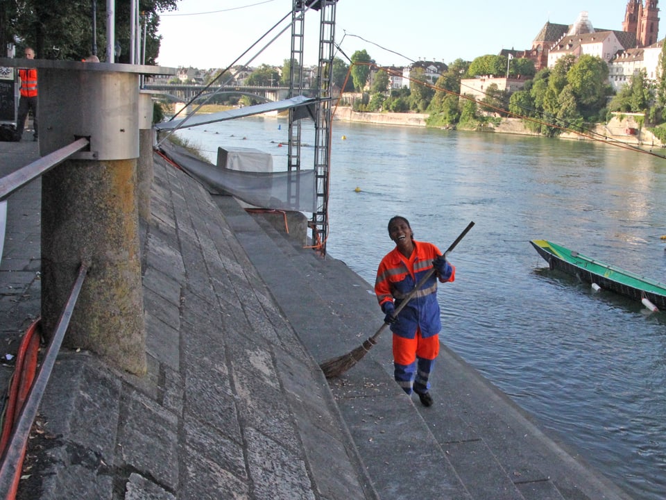 Eine Frau mit Putzanzug wischt das Rheinufer.