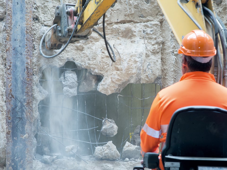 Ein Bauarbeiter schlägt mit seiner Maschine ein Loch in die Wand