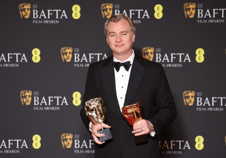 Christopher Nolan mit zwei Preisen in der Hand vor der Bafta-Wand.