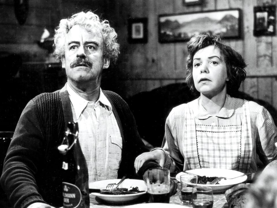 Ein Mann und eine Frau sitzen beim Esstisch und blicken erstaunt von ihren Tellern hoch.