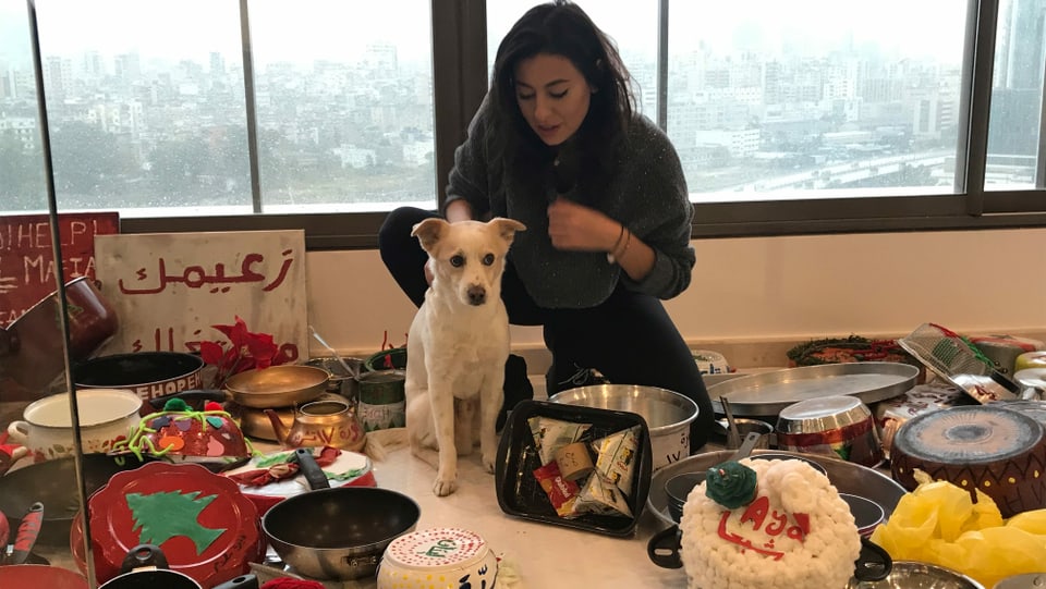 Künstlerin Hayat Nazer mit Hund Pucci in ihrem Atelier in Beirut. Sie hat Libanesinnen und Libanesen aufgefordert, alte Pfannen mit ihrem Namen, Wohnort und ihren Wünschen für Libanon zu  bemalen. Daraus will sie einen Weihnachtsbaum bauen, der ein Zeichen für Einigkeit und Frieden setzt.