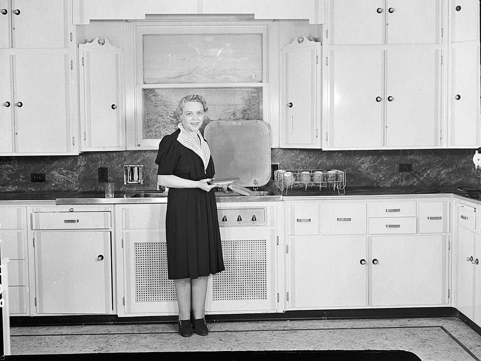 Eine Frau in einem dunklen Kleid posiert in einer weissen Küche.