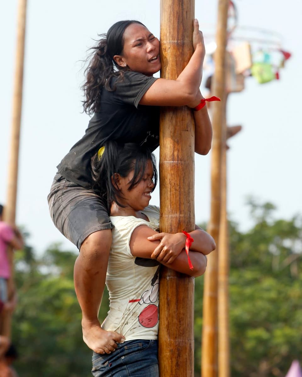 Zwei Frauen klettern im Teamwork den Stamm hoch.
