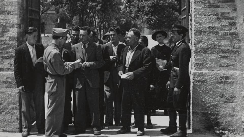 Schwarzweiss-Foto von Männern, welche vor Beamtem warten.