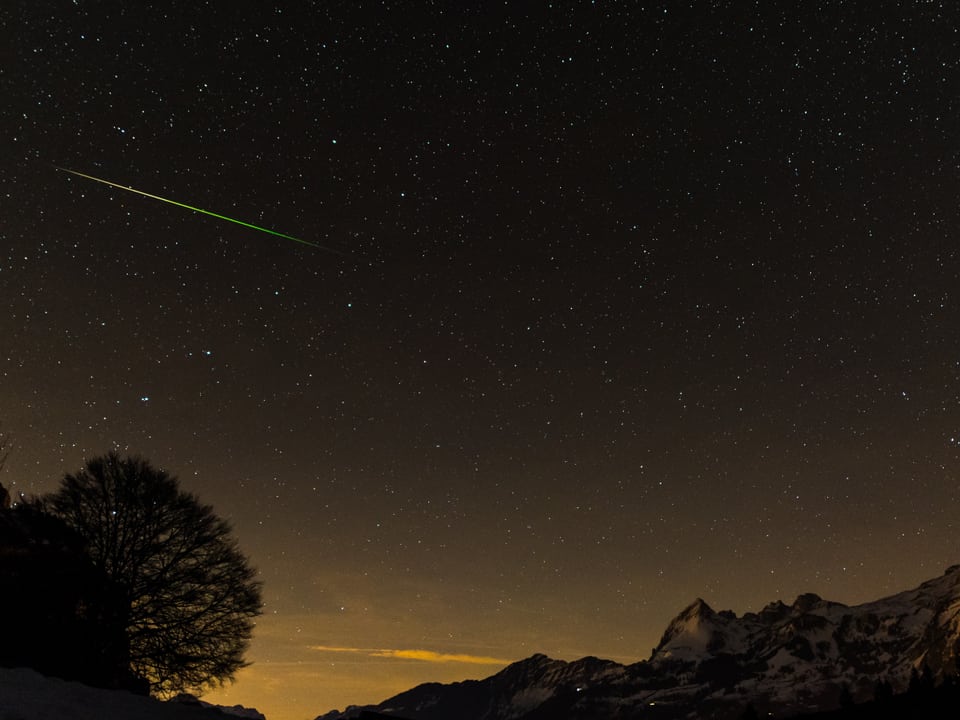 Eine grünliche Sternschnuppe durchzieht den Nachthimmel.