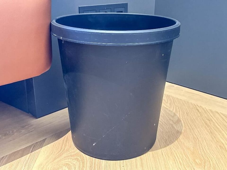 Ein blauer Abfalleimer aus Plastik steht auf einem Holzboden