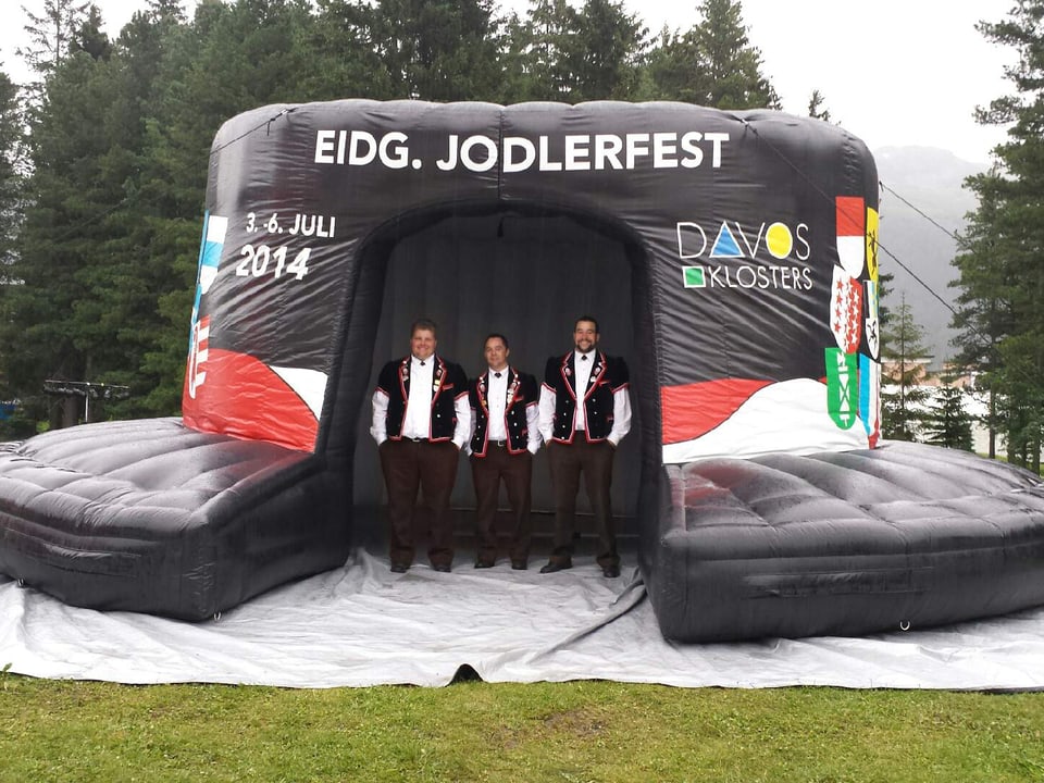 Die drei Jodler posieren unter einem aufgeblasenen schwarzen Hut, dem Kennzeichen des Jodlerfests.