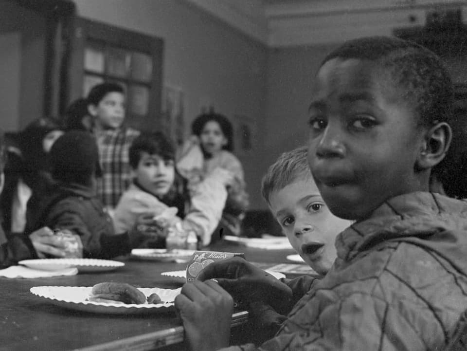 Kinder sitzen auf einem Tisch und essen.