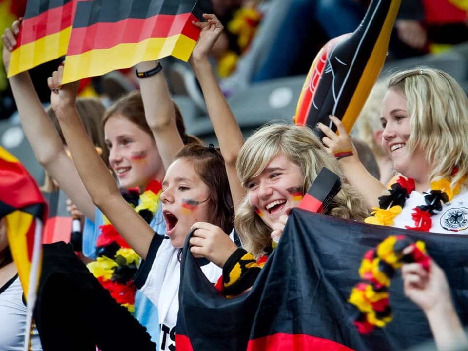 Freudige deutsche Fussballfans mit Flaggen und Schals im Stadion.