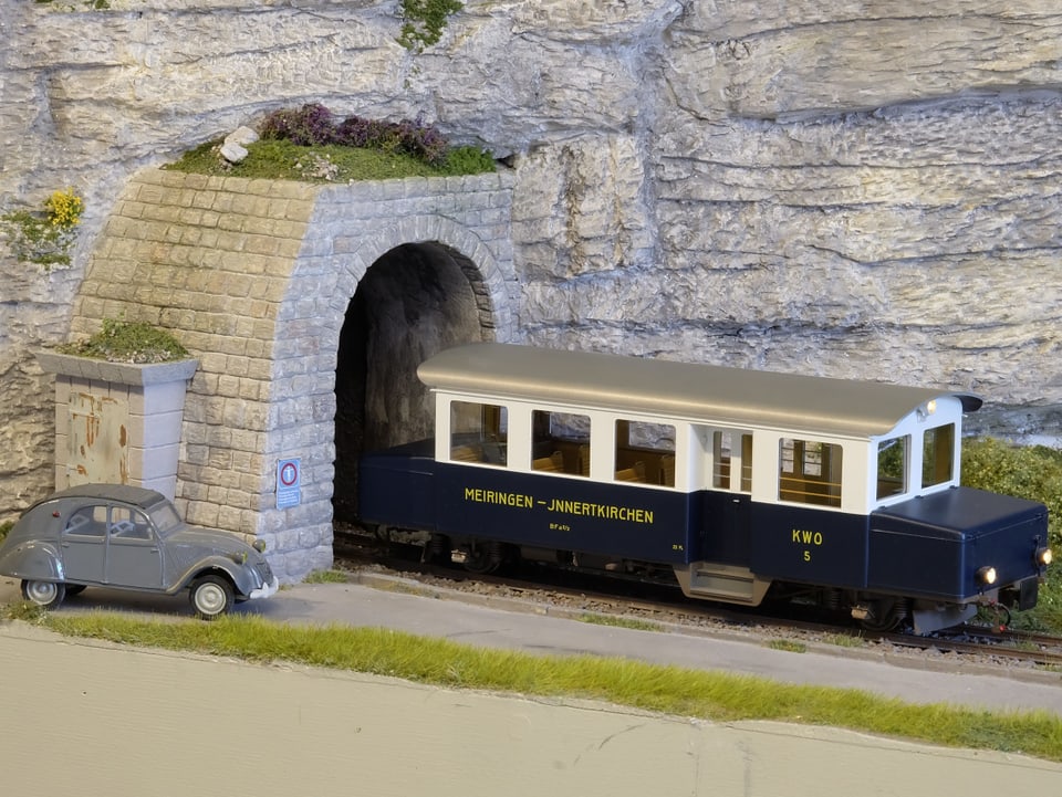 Ein Modelleisenbahnwagen fährt aus einem Tunnel.