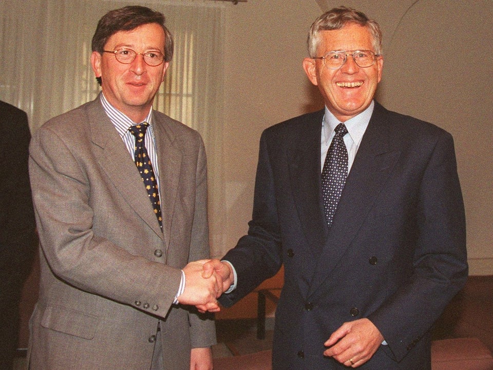 Jean-Claude Juncker und Kaspar Villiger schütteln die Hände und lächeln in die Kamera.
