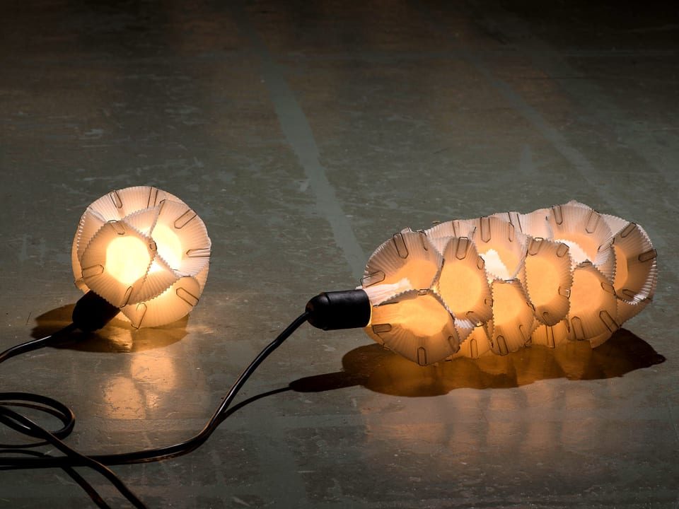 Eine Lampe bestehend aus weissen Muffin-Förmchen, die mit Büroklammern zusammengehalten sind.