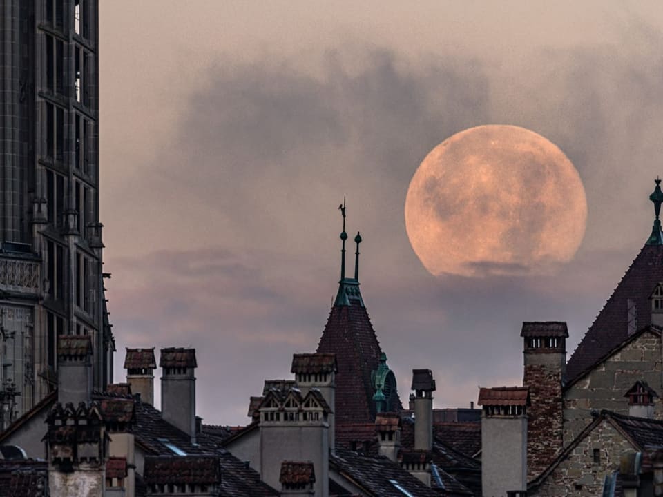 Blick über die Dächer der Altstadt von Bern auf den grossen und hellen Vollmond am lila Himmel.