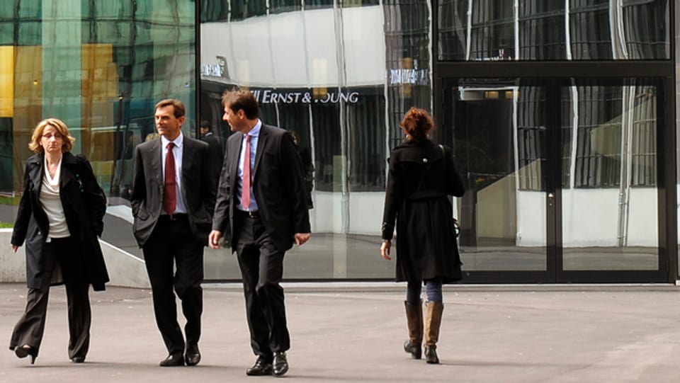 Eine Frau und zwei Männer laufen weg von einem E&Y Gebäude. 