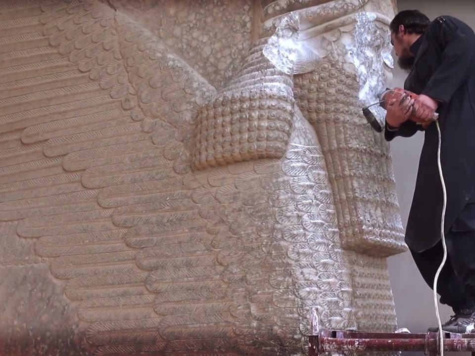 Ein IS-Anhänger zerstört eine grosse Figur über einem Torbogen.