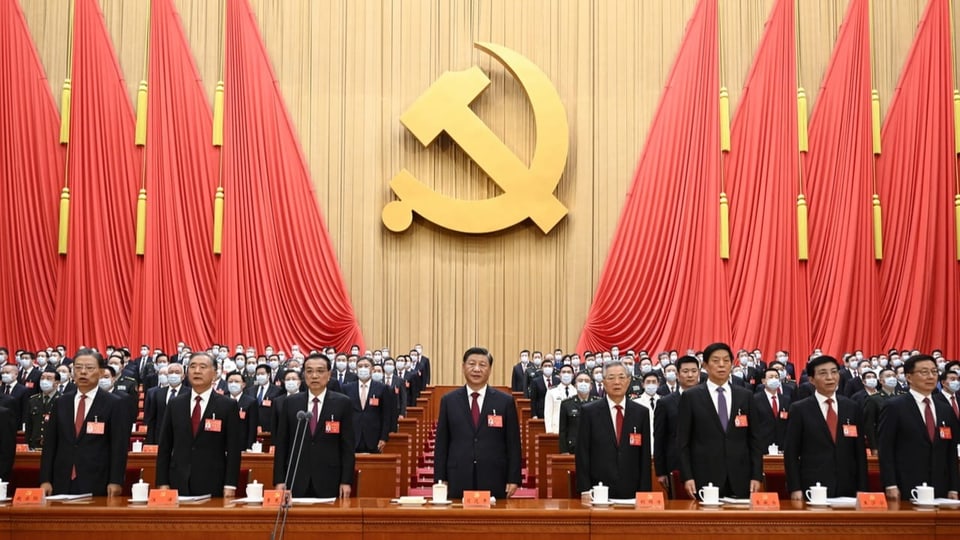 Xi Jinping (Mitte) umgeben von Delegierten der Kommunistischen Partei, im Hintergrund Hammer und Sichel und rote Flaggen