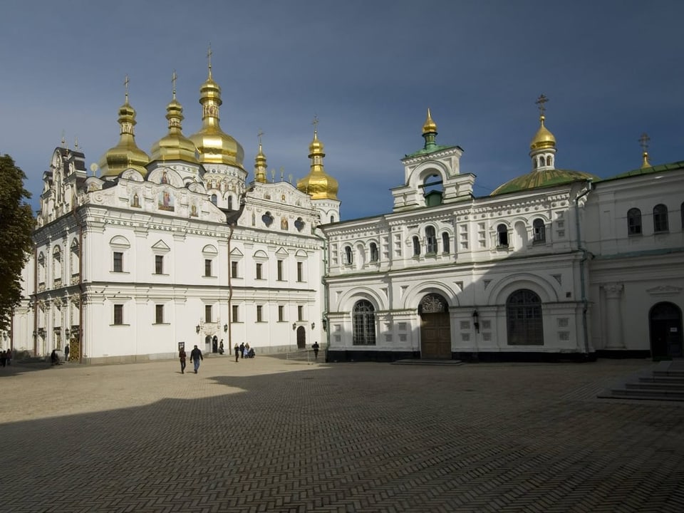 Kloster mit goldenen Zwiebelkuppeln, davor grosser Platz, nur wenige Menschen. Die Fassade des Klosters ist weiss.