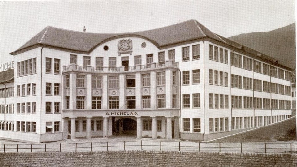 Schwarzweiss-Aufnahme eines Fabrikgebäudes mit Säulen und Uhr.