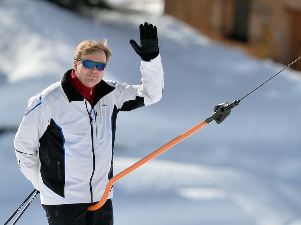 Willem-Alexander in weisser Jacke auf dem Skilift. Er winkt. 