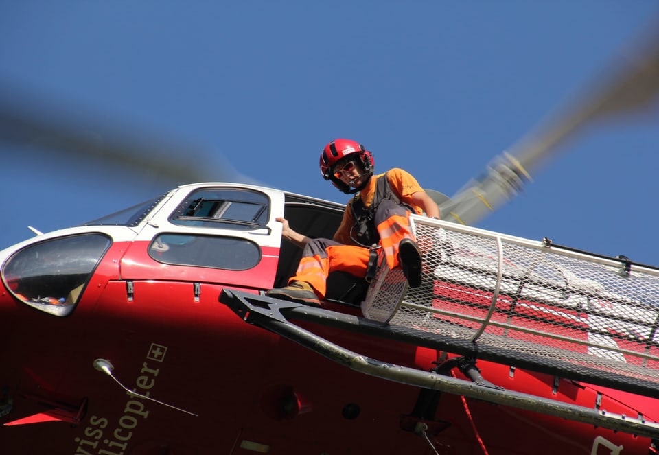 Ein Mitarbeiter steht auf einem Aussengitter des Hubschraubers in luftiger Höhe.