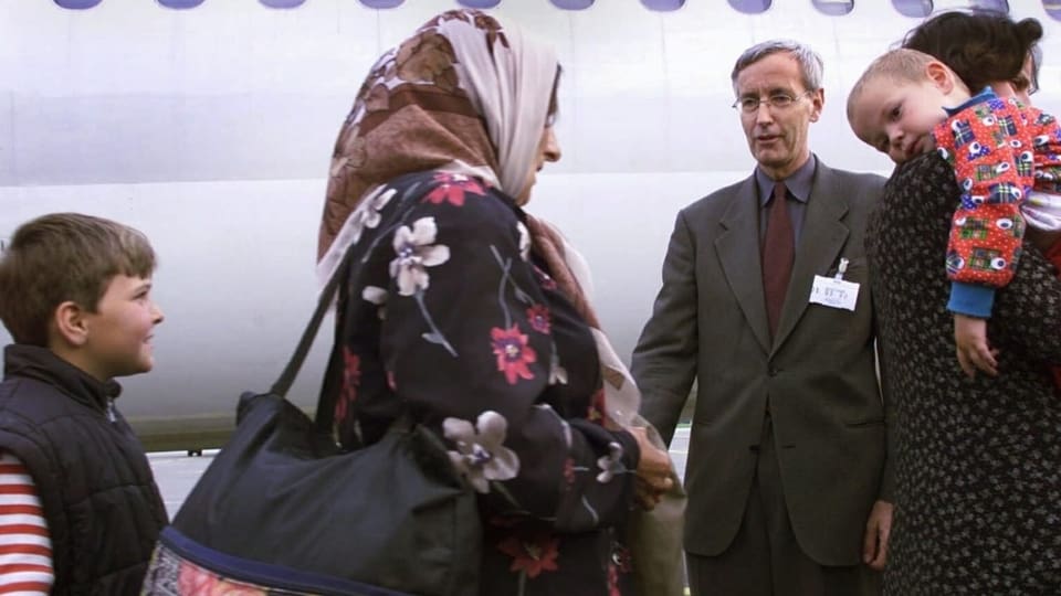 Ein Mann begrüsst vor einem Flugzeug zwei Flüchtlingsfamilien.