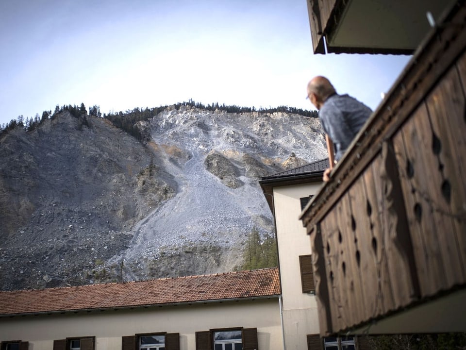 Ein Mann auf einem Balkon blickt Richtung Berg, wo bereits einiges an Geröll zu Tal gedonnert ist.