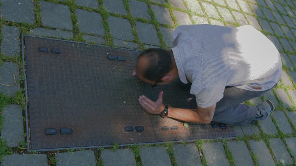 SRF Digital-Mann Reto Widmer kniend auf dem rostigen Schacht, der das Bodensee-Glasfaserkabel abdeckt.