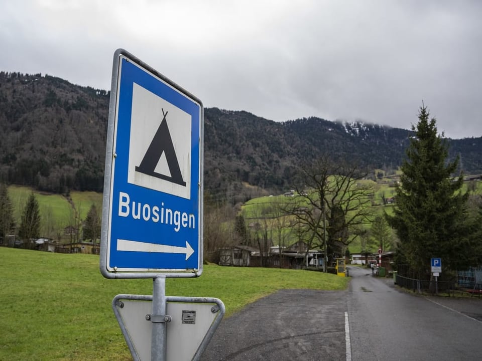 Verkehrsschild Richtung Buosingen mit Zelt-Symbol vor ländlicher Strasse und bewaldeten Hügeln.