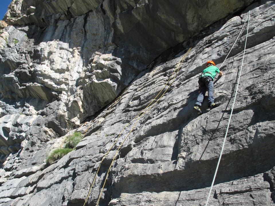 Kind in einer steilen Felswand an einem Seil gesichert. 