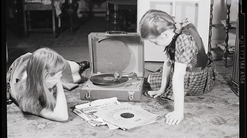 Zwei Mädchen auf einem Schwarz-weiss-Bild hören Schallplatten am Boden.