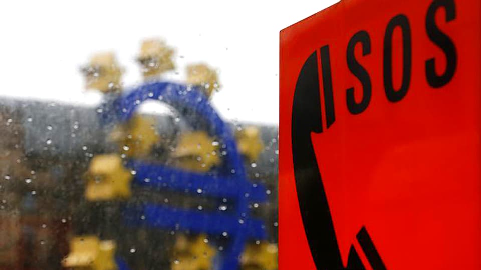 Im Bildvordergrund ist eine SOS-Tafel zu sehen. Dahinter, etwas unscharf, das Euro-Emblem.