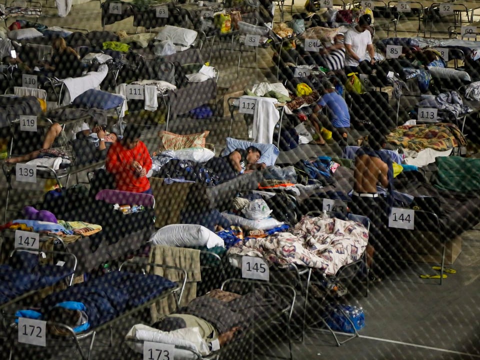 Menschen, die haben fliehen müssen, liegen auf Pritschen in einer Turnhalle.