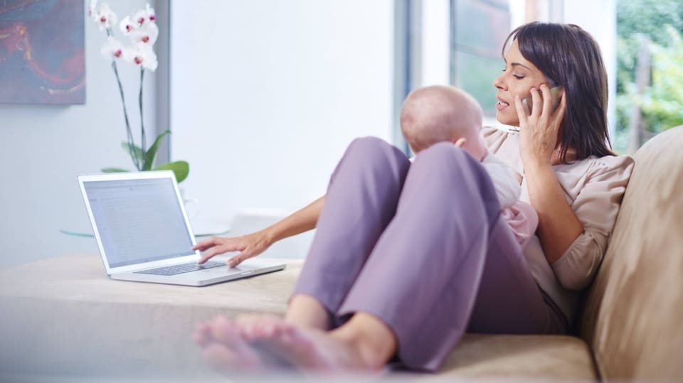 Eine Frau mit einem Kleinkind und an einem Laptop.