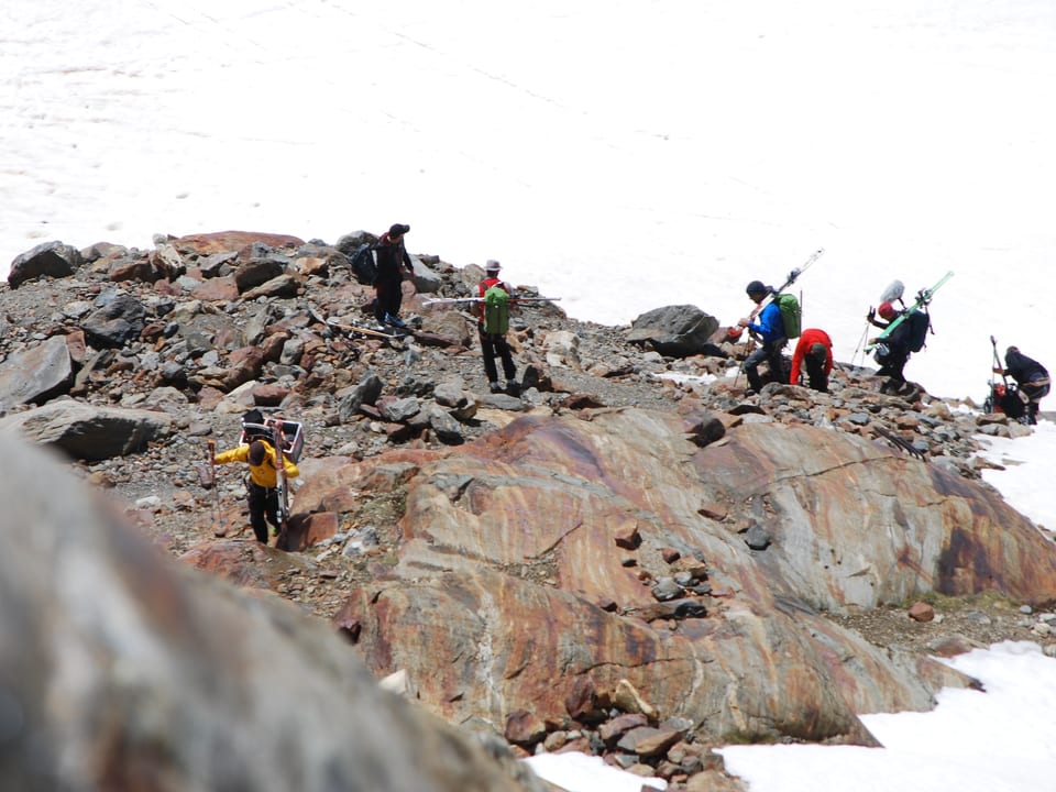 Sieben Personen schleppen Skis und technisches Material den Berg hoch. 