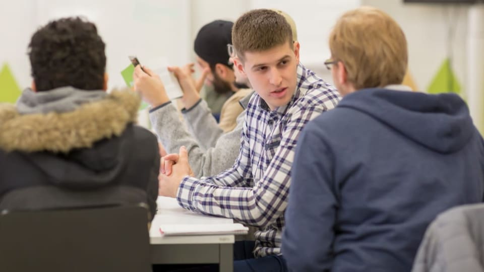 Junge Männer sitzen an einem Tisch und unterhalten sich miteinander. 