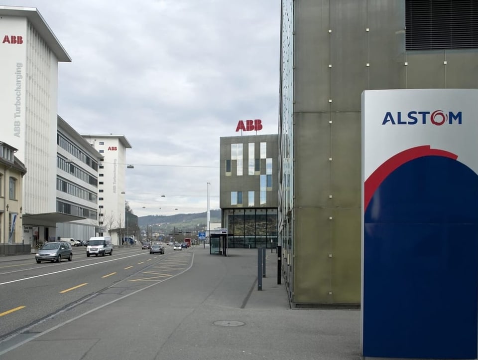 Logo-Tafel Alstom; im Hintergrund sind Gebäude mit der Aufschrift ABB zu sehen
