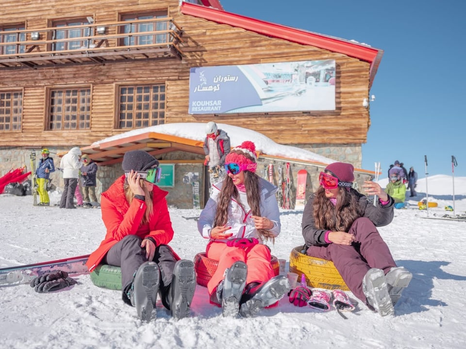 Frauen im Iran sitzen im Schnee in einem Skigebiet.