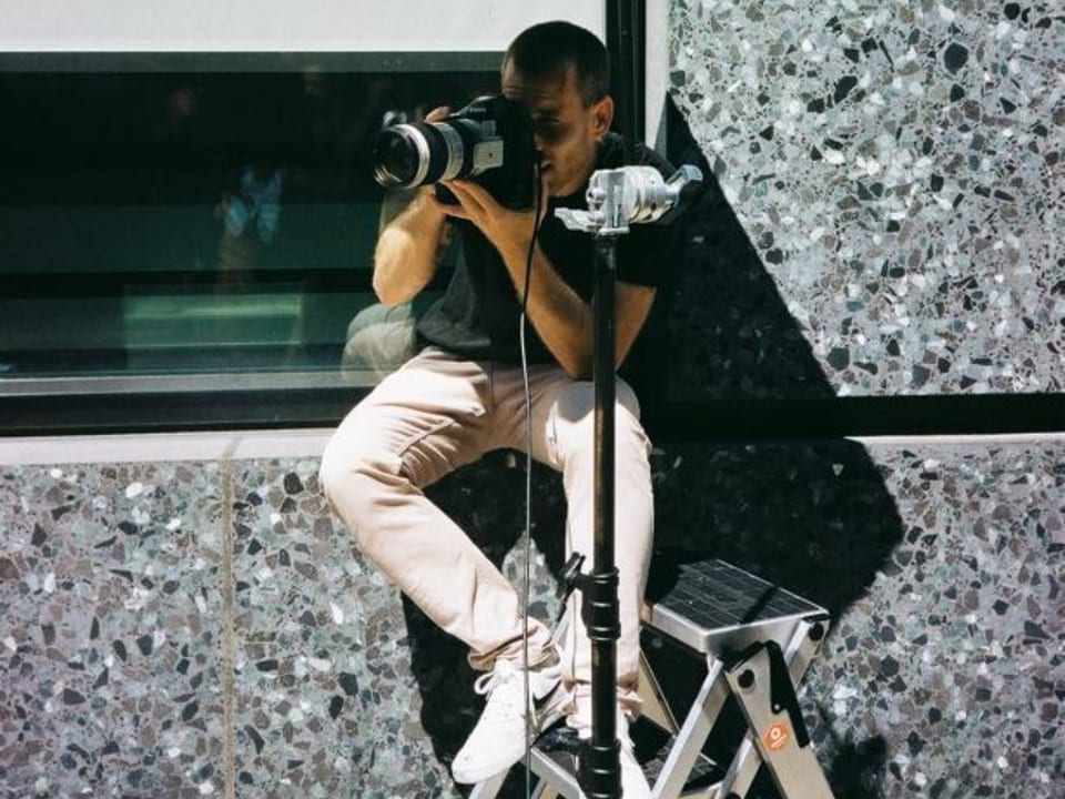Lukas Maeder sitzt vor einem Schaufenster mit seiner Kamera.