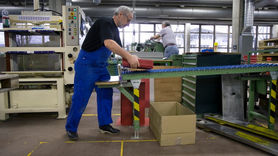 Arbeiter nimmt in einer Fabrikhalle etwas vom Rollband 