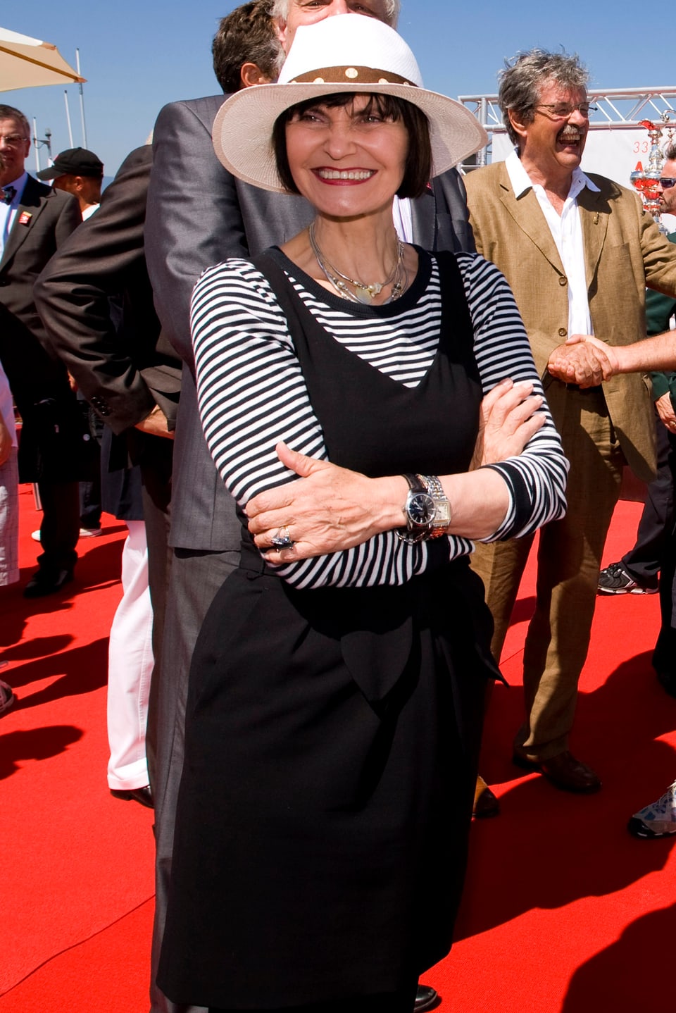 Micheline Calmy-Rey mit Hut, schwarzem Kleid und weiss schwarz gestreiftem Langarm-Shirt unter dem Kleid