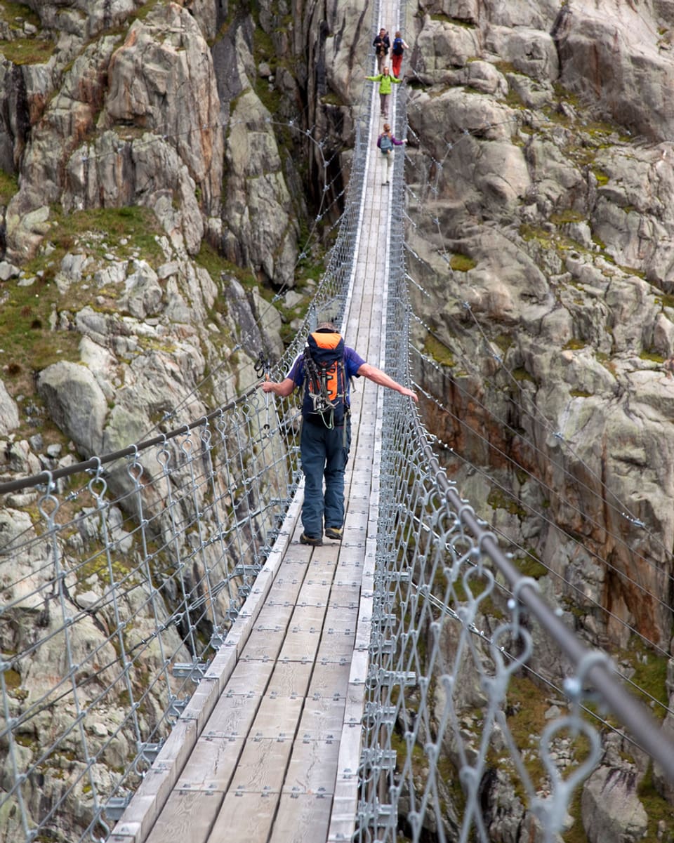 Ein Bergwanderer geht vorsichtig über die längste Hängebrücke im Alpenraum über dem Triftgletscher im Berner Oberland.