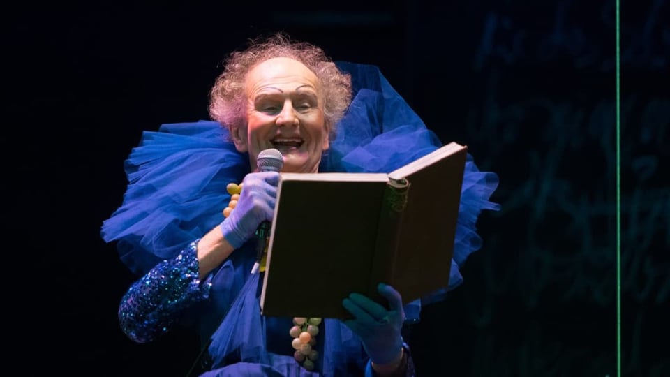 Älterer Herr mit Makeup in Tüllkleid liest aus Buch