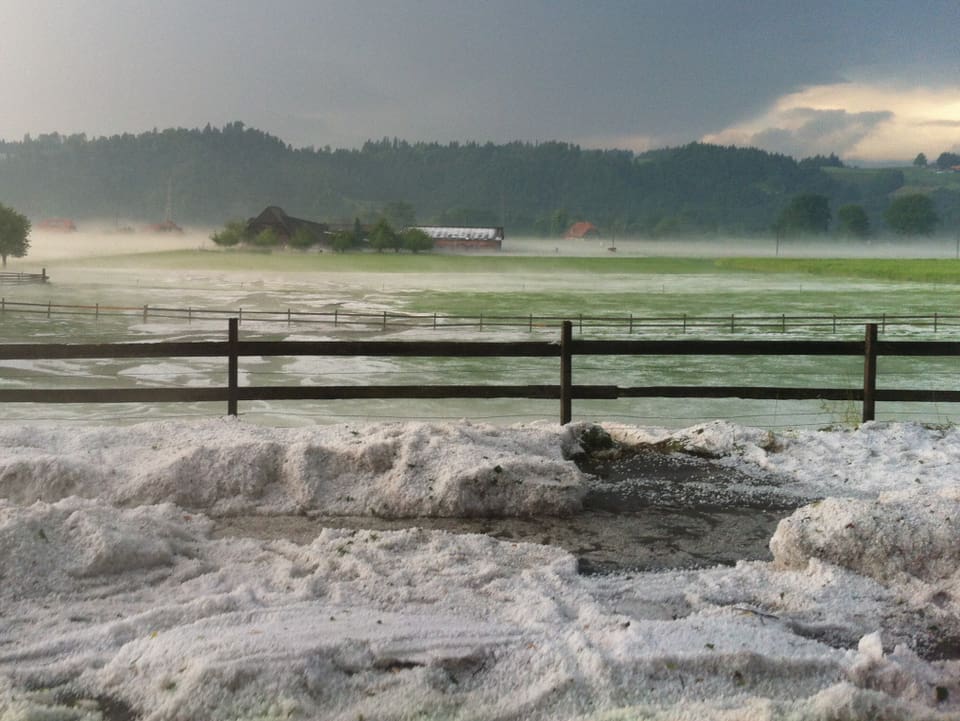 Wiese und Parkplatz, die voller Hagel sind, er liegt wie Schnee da, einige Zentimeter hoch. 