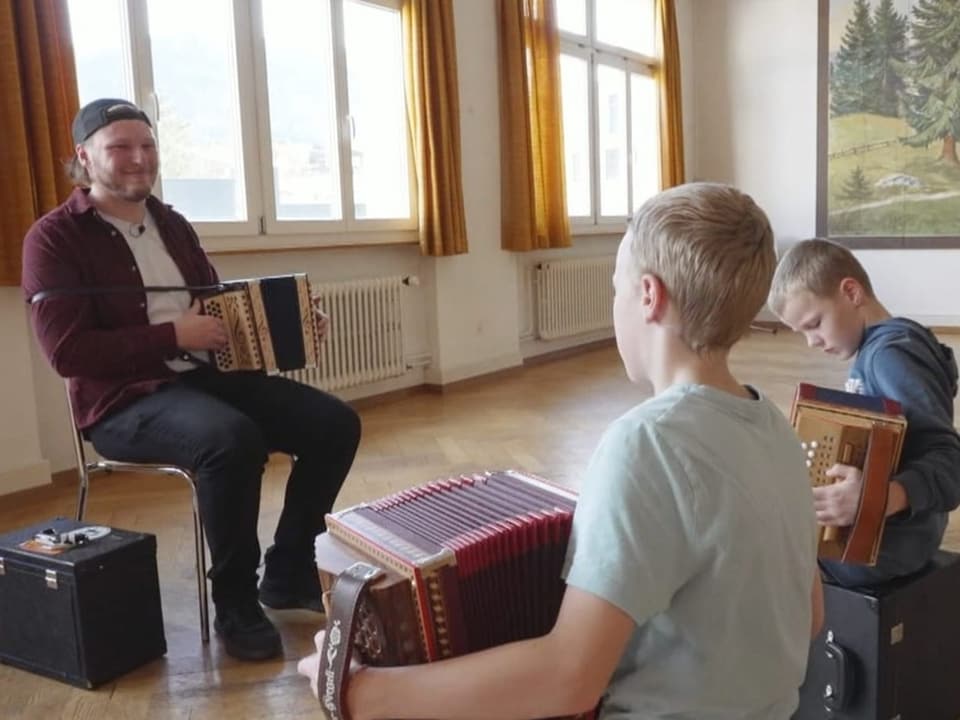 Mann unterrichtet zwei Kinder im Spielen des Akkordeons in einem hellen Raum.